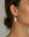 Wiszący kolczyk GOLDEN SAND SHELLS z naturalną muszlą w uchu modelki.png